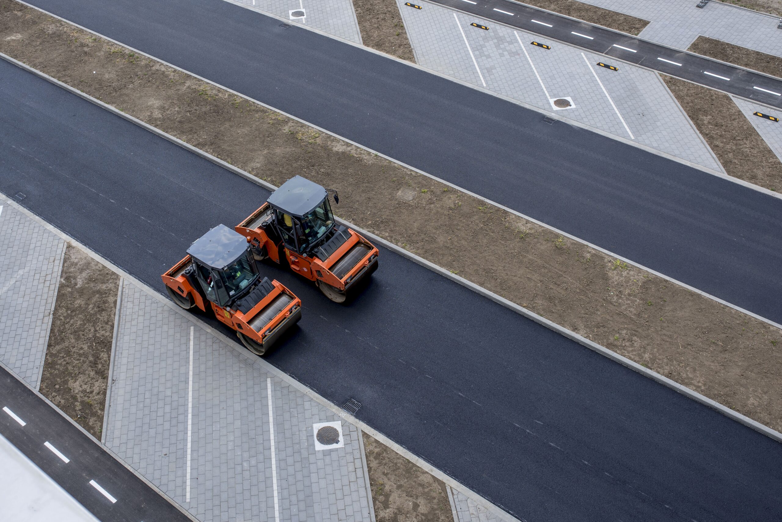 Aerial view of orange vibratory asphalt roller compactor on a new pavement